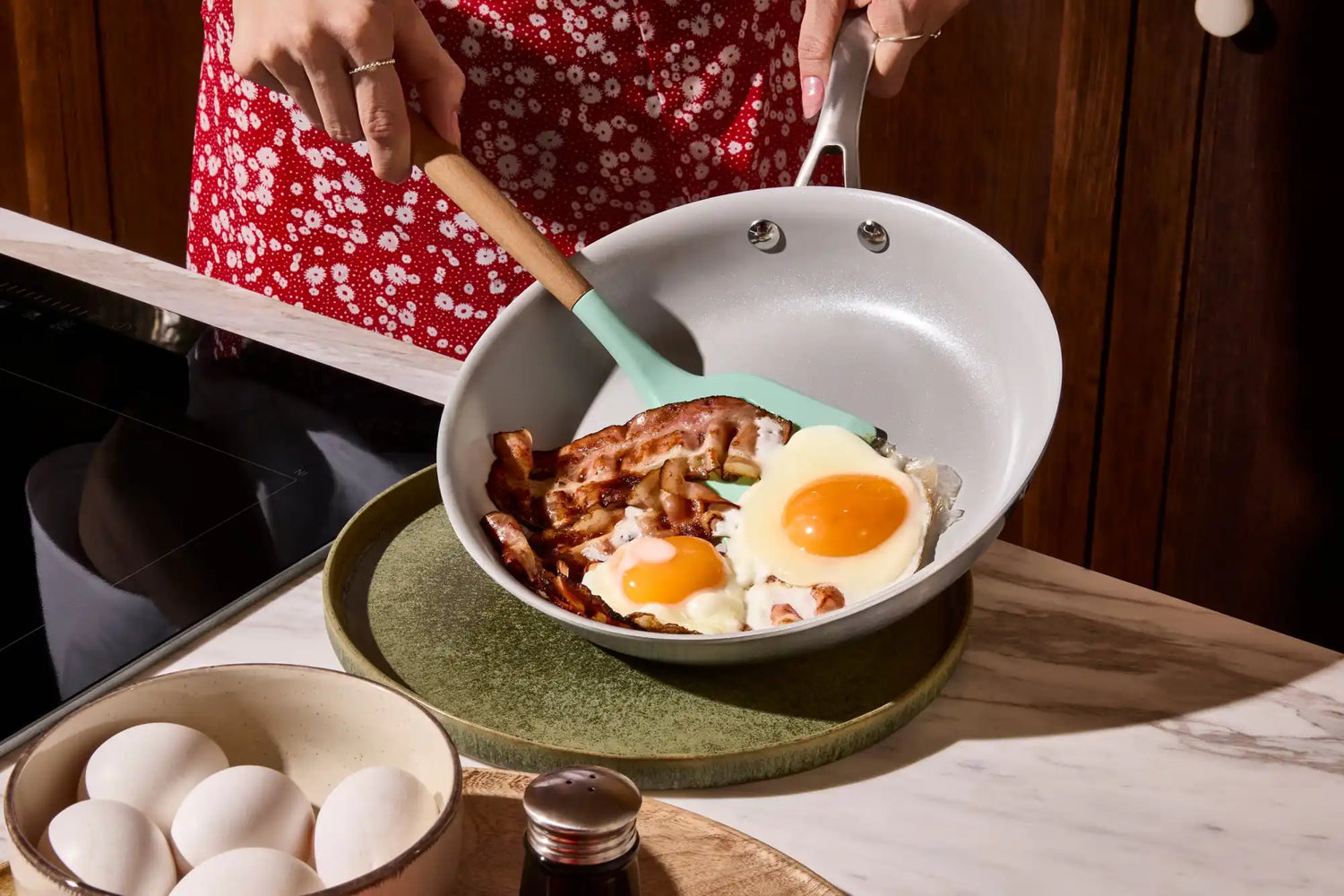 Keramická pánev ve stylu 50. let s dřevěnou rukojetí a tyrkysovou silikonovou stěrkou.